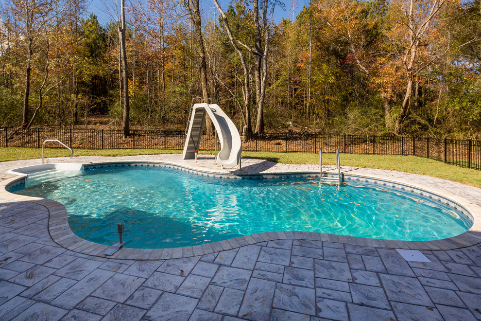 Inspiration for a mid-sized arts and crafts backyard custom-shaped pool in Other with a water slide and stamped concrete.