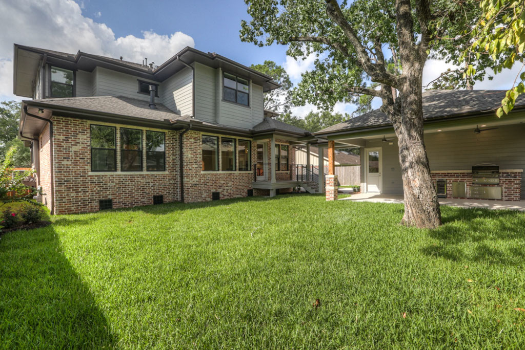 This is an example of a large midcentury two-storey brick grey house exterior in Houston with a hip roof and a shingle roof.