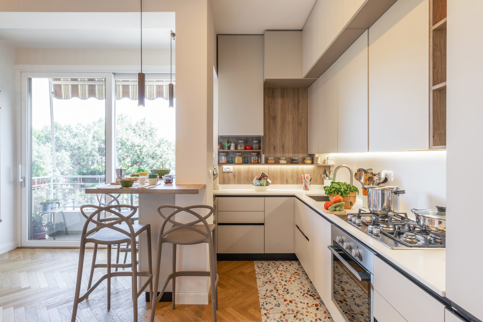 This is an example of a small contemporary u-shaped open plan kitchen in Florence with a submerged sink, flat-panel cabinets, white cabinets, quartz worktops, engineered quartz splashback, stainless steel appliances, light hardwood flooring, an island and brown floors.