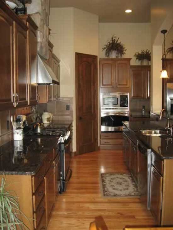 Kitchen pantry - galley medium tone wood floor kitchen pantry idea in Denver with a double-bowl sink, recessed-panel cabinets, dark wood cabinets, granite countertops, brown backsplash, ceramic backsplash and stainless steel appliances