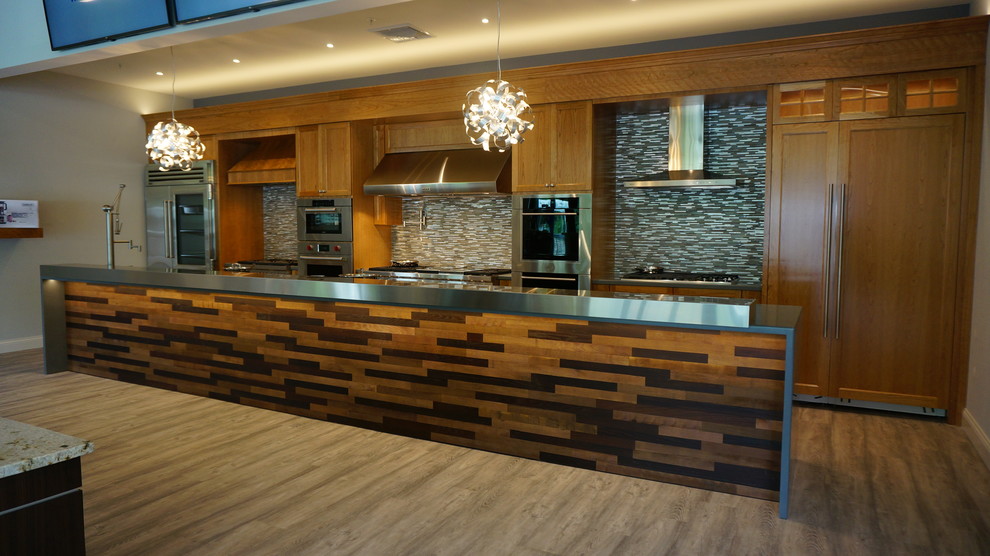Example of a huge transitional single-wall light wood floor kitchen design in Boston with an integrated sink, medium tone wood cabinets, granite countertops, metallic backsplash, stone tile backsplash, stainless steel appliances and an island