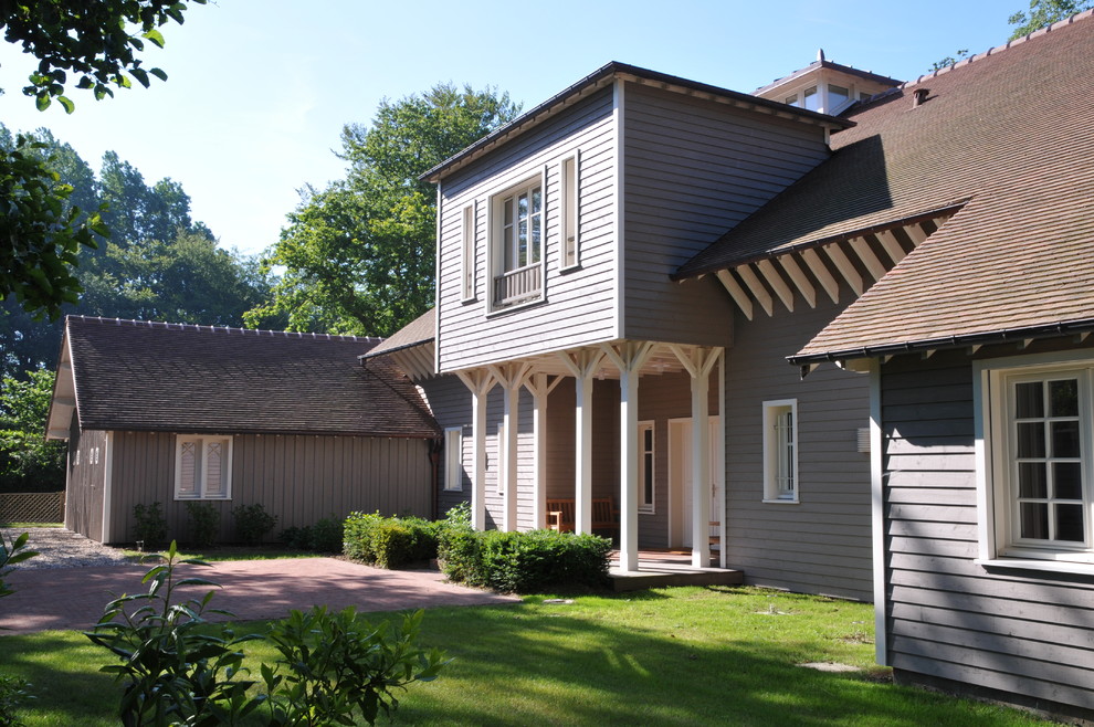 Photo of an expansive grey house exterior in Paris with wood siding, a gable roof and a tile roof.