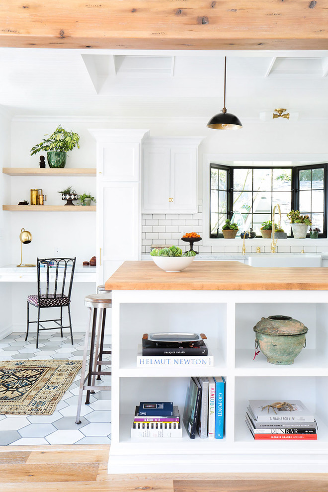 This is an example of a mid-sized scandinavian open plan kitchen in Los Angeles with a farmhouse sink, recessed-panel cabinets, white cabinets, white splashback, subway tile splashback, stainless steel appliances, porcelain floors, a peninsula and wood benchtops.