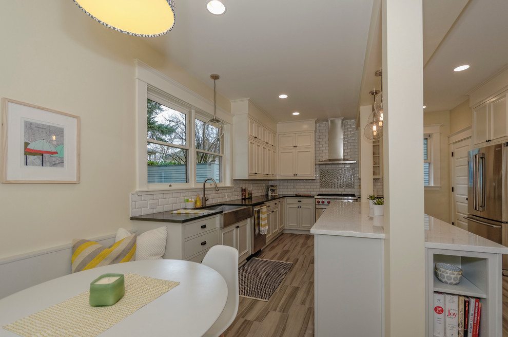 Photo of an expansive transitional eat-in kitchen in Portland with a farmhouse sink, raised-panel cabinets, white cabinets, quartzite benchtops, white splashback, ceramic splashback, stainless steel appliances and porcelain floors.