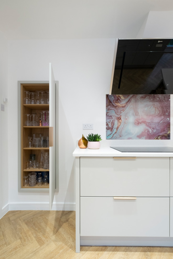 This is an example of a mid-sized contemporary u-shaped eat-in kitchen in Cardiff with an integrated sink, flat-panel cabinets, pink cabinets, quartzite benchtops, pink splashback, glass sheet splashback, stainless steel appliances, laminate floors, a peninsula and white benchtop.