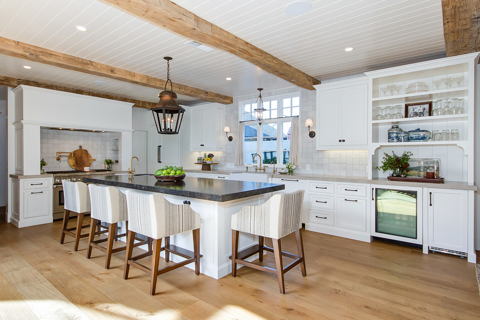 Inspiration for a large country l-shaped eat-in kitchen in Orange County with a farmhouse sink, shaker cabinets, white cabinets, quartzite benchtops, beige splashback, ceramic splashback, stainless steel appliances, light hardwood floors, with island, brown floor and beige benchtop.