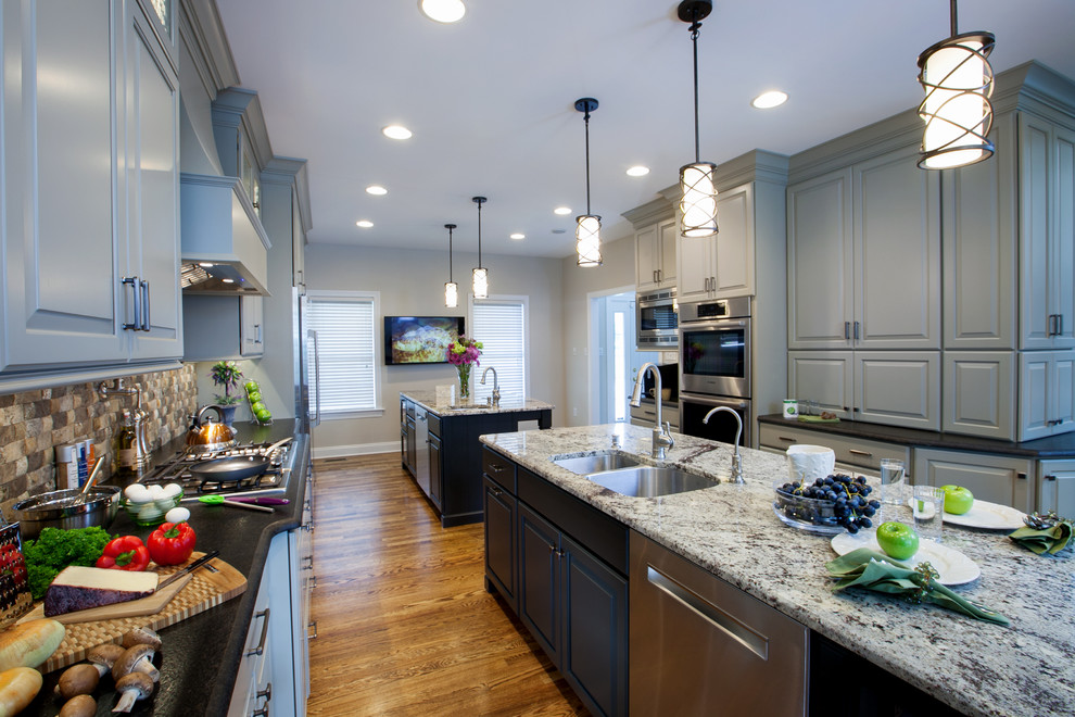 Inspiration for a large transitional galley medium tone wood floor eat-in kitchen remodel with an undermount sink, raised-panel cabinets, gray cabinets, granite countertops, multicolored backsplash, stone tile backsplash, stainless steel appliances and two islands