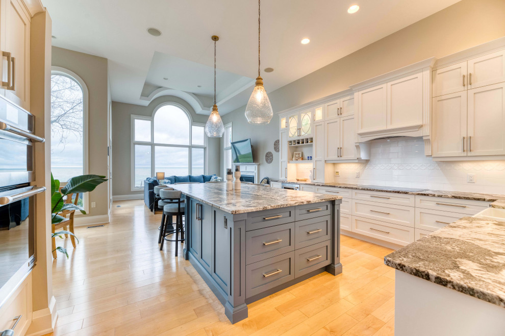 Example of a large transitional l-shaped light wood floor and brown floor eat-in kitchen design with a farmhouse sink, shaker cabinets, white cabinets, granite countertops, ceramic backsplash, stainless steel appliances and an island