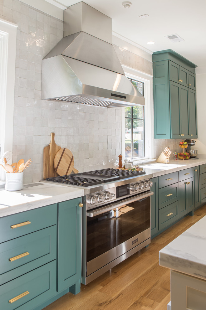 Example of a large transitional u-shaped light wood floor open concept kitchen design with an undermount sink, shaker cabinets, green cabinets, quartz countertops, white backsplash, stainless steel appliances and an island