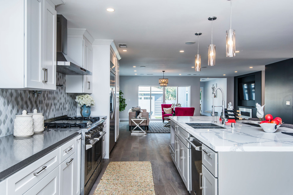 This is an example of a mid-sized contemporary galley open plan kitchen in Los Angeles with a double-bowl sink, shaker cabinets, white cabinets, marble benchtops, grey splashback, stainless steel appliances, dark hardwood floors, with island, brown floor and white benchtop.