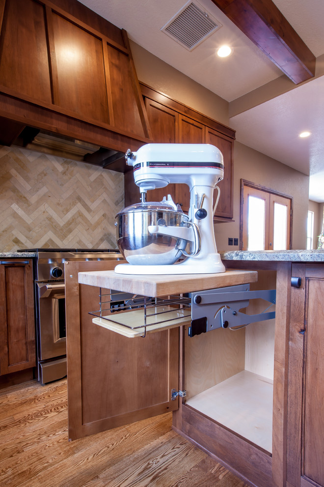 Mid-sized mountain style u-shaped medium tone wood floor and brown floor enclosed kitchen photo in Omaha with an undermount sink, shaker cabinets, dark wood cabinets, granite countertops, beige backsplash, travertine backsplash, stainless steel appliances, an island and multicolored countertops