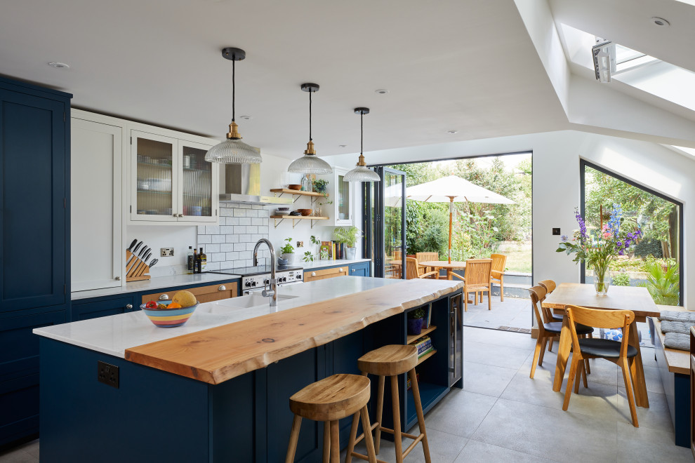 Inspiration for a mid-sized transitional single-wall eat-in kitchen in London with a farmhouse sink, shaker cabinets, blue cabinets, quartzite benchtops, white splashback, ceramic splashback, stainless steel appliances, porcelain floors, with island, grey floor, grey benchtop and vaulted.