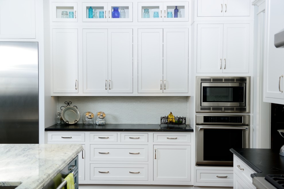 This is an example of a large transitional l-shaped eat-in kitchen in Raleigh with white cabinets, soapstone benchtops, white splashback, glass tile splashback, stainless steel appliances, medium hardwood floors, with island and brown floor.