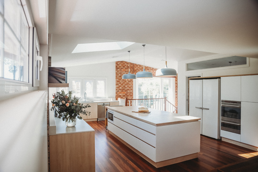 Large contemporary l-shaped eat-in kitchen in Canberra - Queanbeyan with an undermount sink, flat-panel cabinets, light wood cabinets, wood benchtops, brick splashback, stainless steel appliances, dark hardwood floors, with island and beige benchtop.
