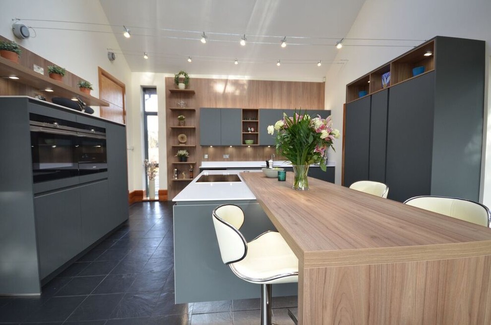 Photo of a mid-sized contemporary u-shaped eat-in kitchen in Glasgow with grey cabinets, black appliances, with island, a double-bowl sink, flat-panel cabinets, wood benchtops, black splashback, timber splashback, medium hardwood floors and black floor.