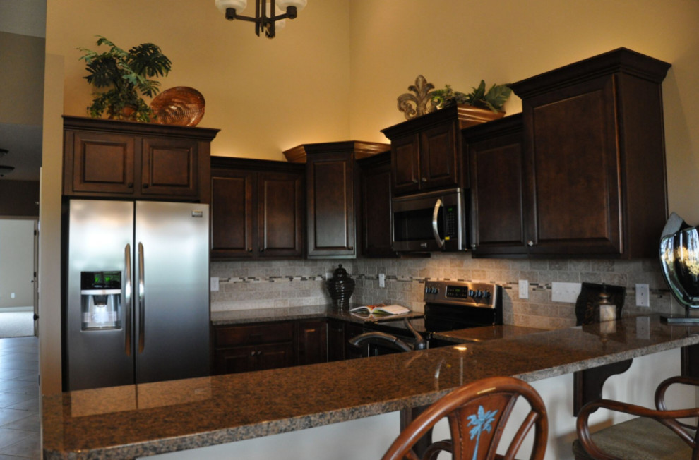 Inspiration for a mid-sized timeless u-shaped eat-in kitchen remodel with raised-panel cabinets, brown cabinets, granite countertops, beige backsplash, stone tile backsplash, stainless steel appliances and a peninsula