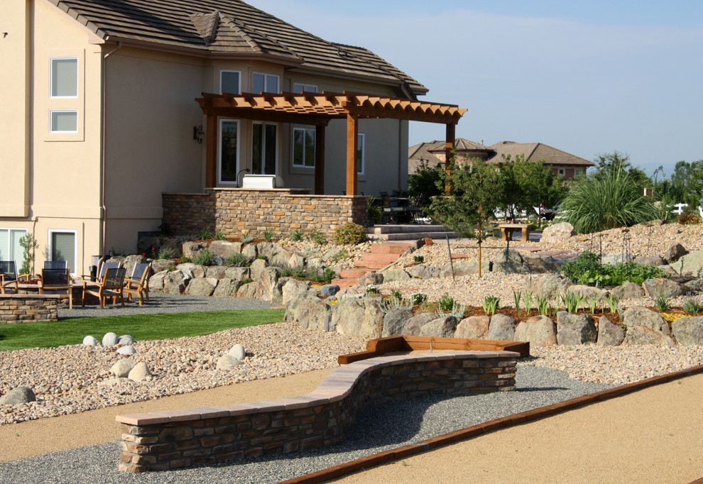 This is an example of an eclectic backyard garden in Denver with a water feature and natural stone pavers.