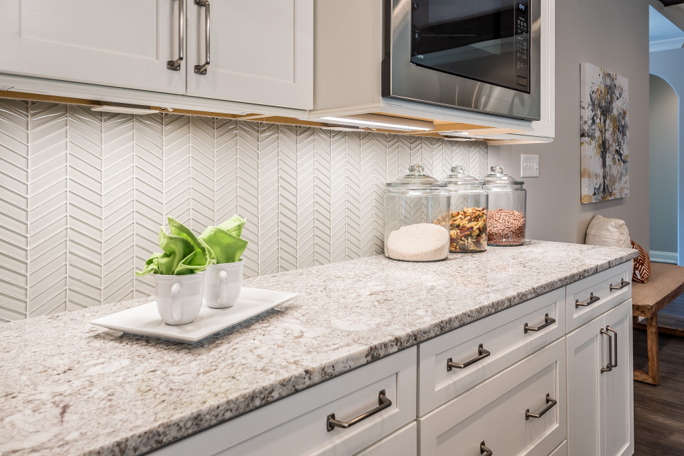 Mid-sized transitional l-shaped open concept kitchen photo with an undermount sink, flat-panel cabinets, white cabinets, quartz countertops, white backsplash, glass tile backsplash, stainless steel appliances, an island and white countertops