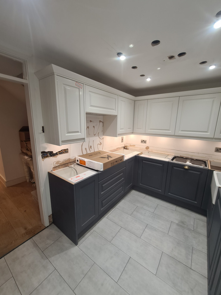 ロンドンにある高級な広いヴィクトリアン調のおしゃれなキッチン (エプロンフロントシンク、シェーカースタイル扉のキャビネット、白いキャビネット、珪岩カウンター、白いキッチンパネル、セラミックタイルのキッチンパネル、パネルと同色の調理設備、セラミックタイルの床、グレーの床、白いキッチンカウンター) の写真
