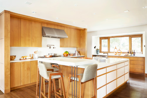 Bright modern kitchen with wood and white kitchen cabinet design, large island with seating, and wide window overlooking the backyard.