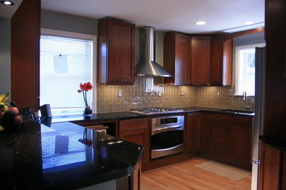 This is an example of a large traditional u-shaped eat-in kitchen in DC Metro with an undermount sink, black cabinets, beige splashback, cement tile splashback, stainless steel appliances, light hardwood floors and with island.