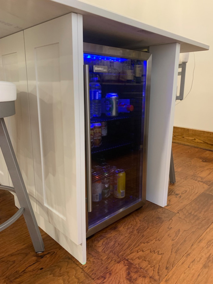 Example of a small transitional galley medium tone wood floor open concept kitchen design in Toronto with shaker cabinets, white cabinets, solid surface countertops, an island and white countertops