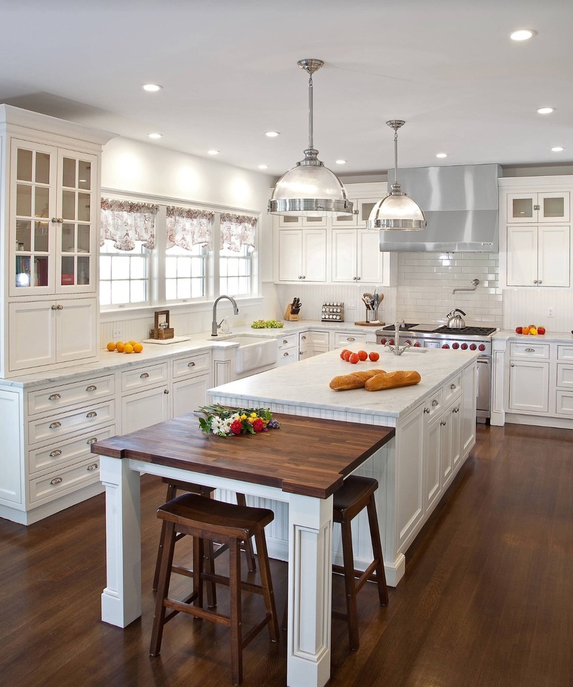 Design ideas for a traditional u-shaped kitchen in San Francisco with a farmhouse sink, shaker cabinets, white cabinets, white splashback, subway tile splashback, stainless steel appliances, dark hardwood floors and with island.
