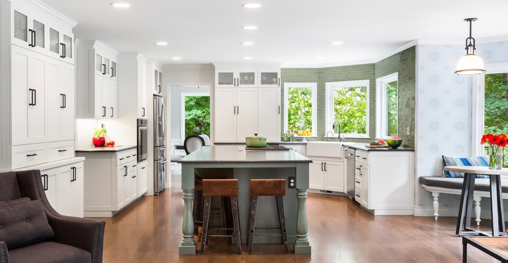 Mid-sized country u-shaped open plan kitchen in Seattle with a farmhouse sink, shaker cabinets, green cabinets, soapstone benchtops, green splashback, ceramic splashback, stainless steel appliances, medium hardwood floors, with island and brown floor.