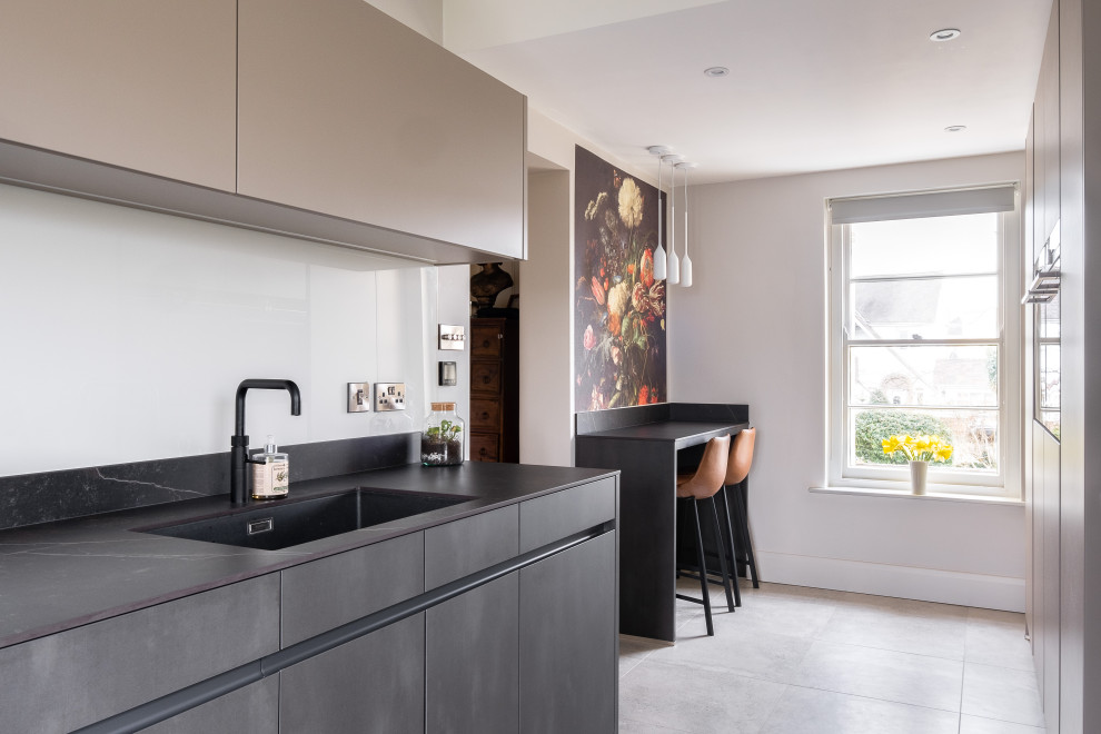 Photo of a small contemporary galley separate kitchen in Gloucestershire with a drop-in sink, flat-panel cabinets, solid surface benchtops, black appliances, porcelain floors, grey floor and black benchtop.