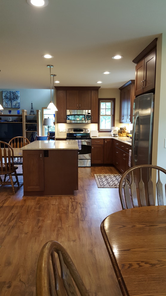 Large transitional l-shaped vinyl floor eat-in kitchen photo with an undermount sink, shaker cabinets, dark wood cabinets, quartz countertops, beige backsplash, subway tile backsplash, stainless steel appliances and an island