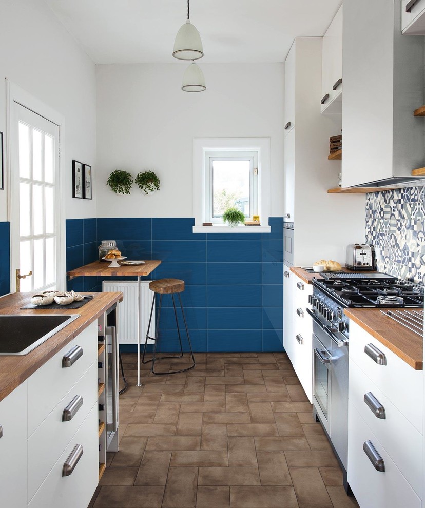 Inspiration for a mediterranean galley kitchen in Other with a drop-in sink, flat-panel cabinets, white cabinets, wood benchtops, multi-coloured splashback, no island, brown floor and brown benchtop.