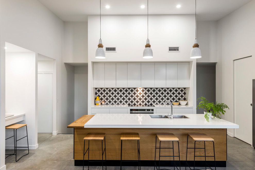 This is an example of a contemporary galley kitchen in Gold Coast - Tweed with a double-bowl sink, flat-panel cabinets, white cabinets, multi-coloured splashback, stainless steel appliances, with island and grey floor.