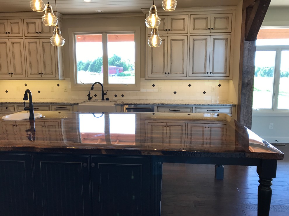 This is an example of a large country u-shaped kitchen pantry in Other with a farmhouse sink, beaded inset cabinets, distressed cabinets, granite benchtops, white splashback, porcelain splashback, stainless steel appliances, dark hardwood floors, with island and brown floor.