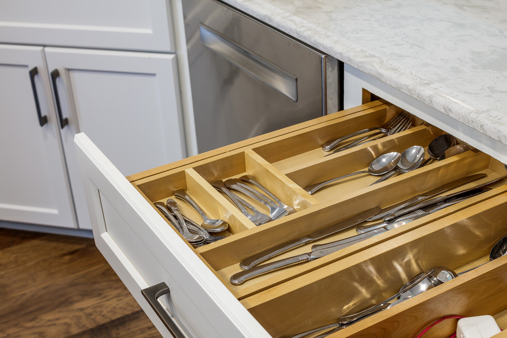 Example of a brown floor eat-in kitchen design with white cabinets, white backsplash, stainless steel appliances, an island and gray countertops