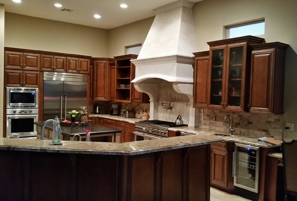 Inspiration for an expansive modern l-shaped eat-in kitchen in Phoenix with an undermount sink, raised-panel cabinets, medium wood cabinets, granite benchtops, beige splashback, stone tile splashback, stainless steel appliances, travertine floors and multiple islands.