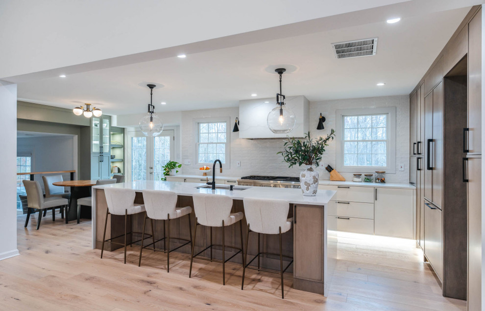 This is an example of a large transitional l-shaped open plan kitchen in DC Metro with a single-bowl sink, shaker cabinets, white cabinets, quartz benchtops, white splashback, porcelain splashback, stainless steel appliances, light hardwood floors, with island, beige floor and white benchtop.