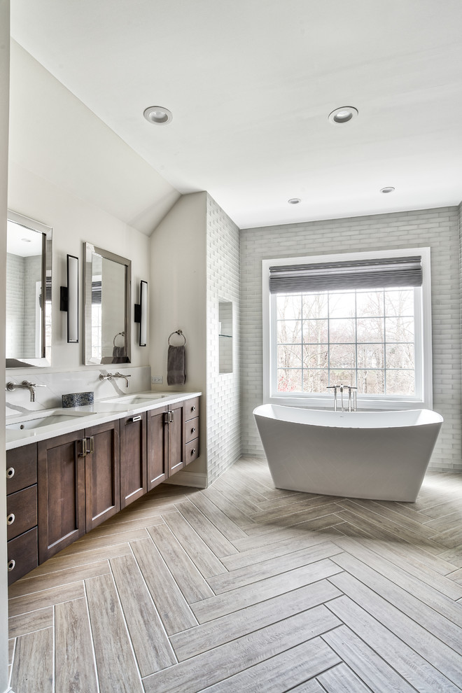 Expansive transitional master bathroom in New York with shaker cabinets, dark wood cabinets, a freestanding tub, an alcove shower, gray tile, glass tile, beige walls, an undermount sink, engineered quartz benchtops, a hinged shower door and white benchtops.