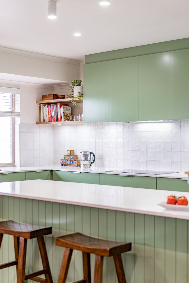 Inspiration for a mid-sized contemporary l-shaped kitchen in Adelaide with a drop-in sink, green cabinets, quartz benchtops, white splashback, porcelain splashback, black appliances, medium hardwood floors, with island and white benchtop.
