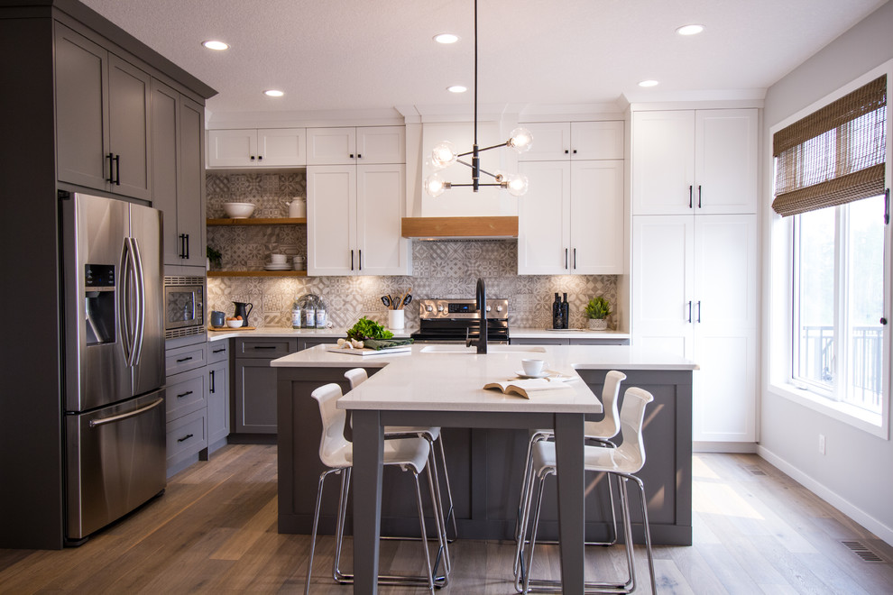 Kitchen - transitional l-shaped medium tone wood floor and brown floor kitchen idea with an undermount sink, shaker cabinets, white cabinets, gray backsplash, stainless steel appliances, an island and white countertops