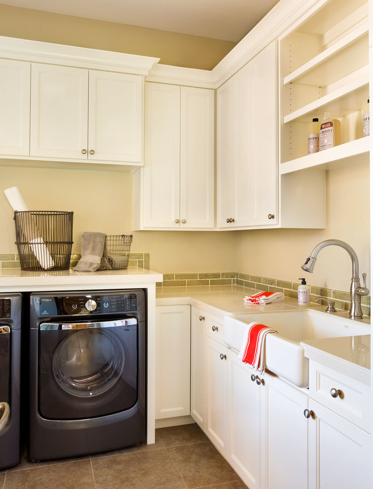 Traditional l-shaped laundry room in Portland with a farmhouse sink, recessed-panel cabinets, white cabinets, beige walls, a side-by-side washer and dryer, brown floor and white benchtop.