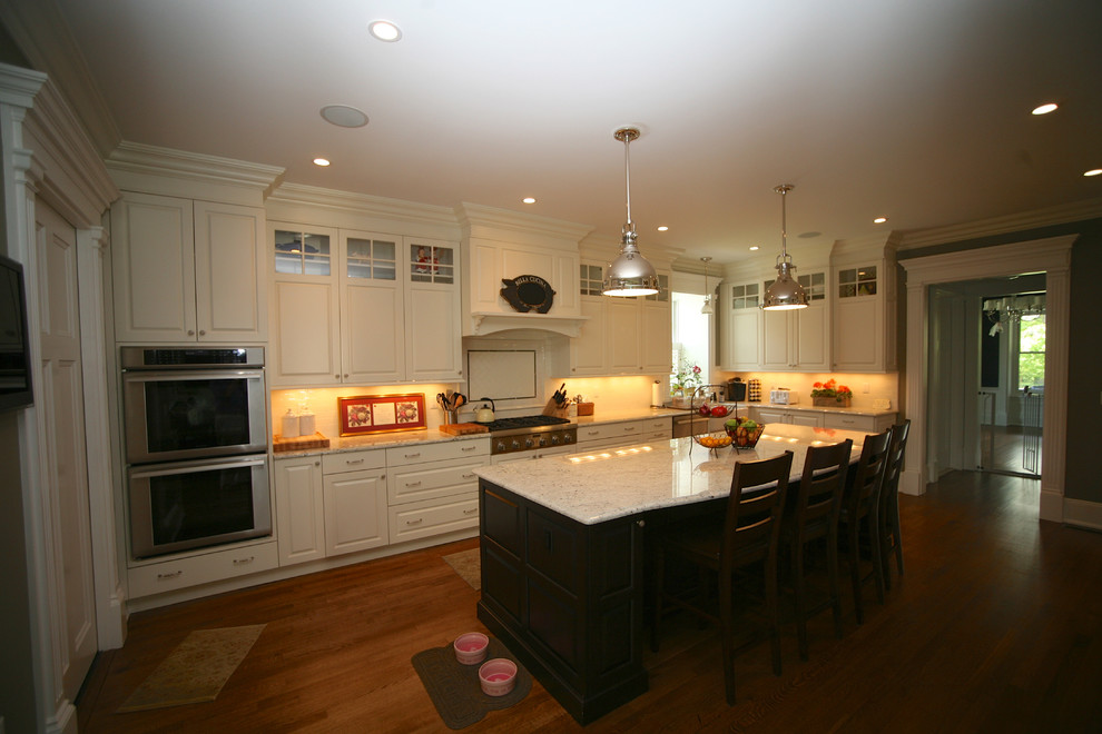 Example of a classic l-shaped eat-in kitchen design in New York with a farmhouse sink, raised-panel cabinets, white cabinets, marble countertops, white backsplash, subway tile backsplash and stainless steel appliances