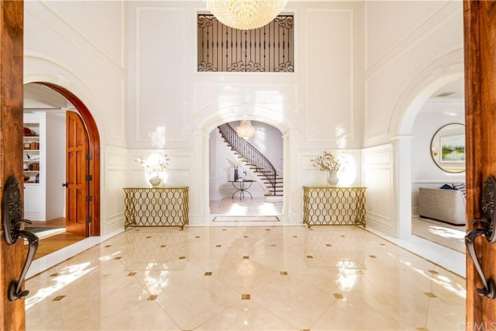 This is an example of a large mediterranean foyer in Los Angeles with white walls, marble flooring, a double front door, a brown front door, a coffered ceiling and panelled walls.