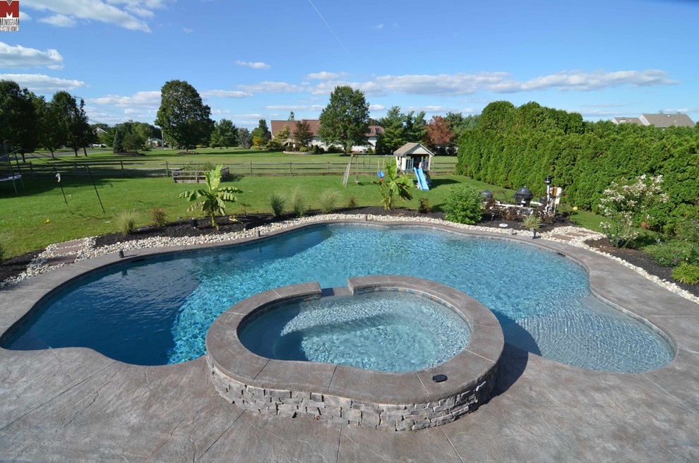 Design ideas for a large contemporary backyard custom-shaped pool in Philadelphia with a hot tub and stamped concrete.