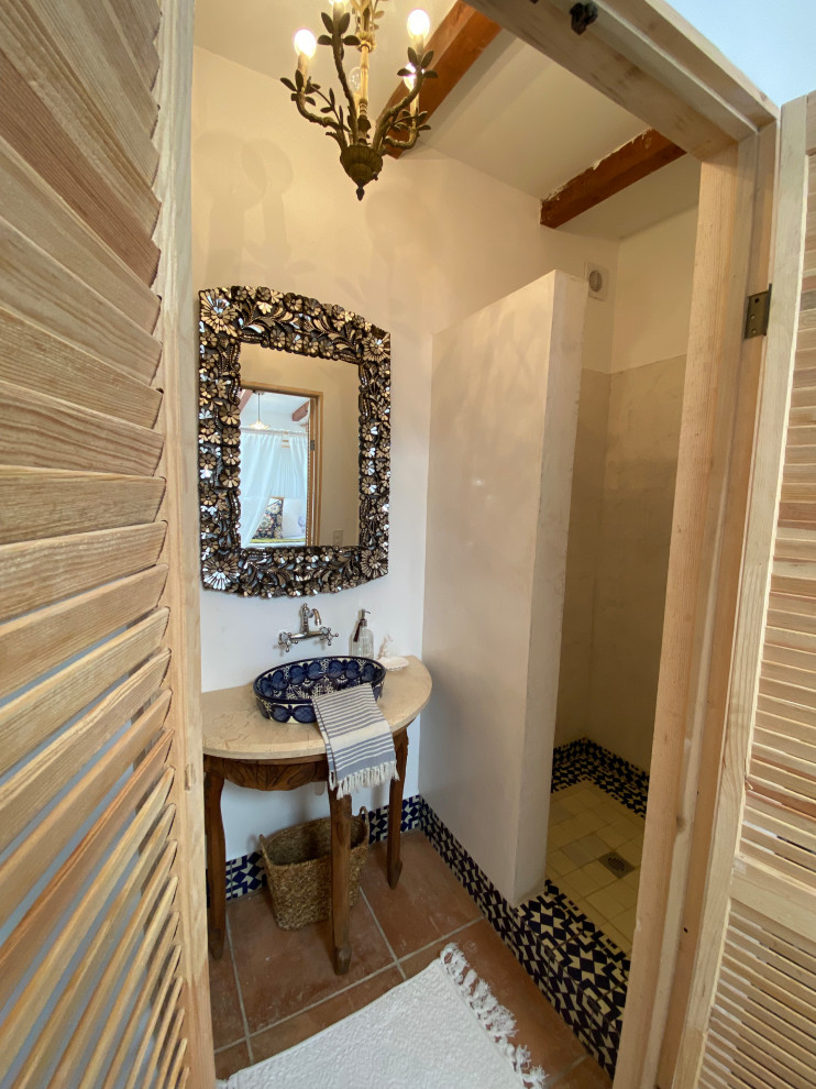 Photo of a small mediterranean 3/4 bathroom in Other with open cabinets, medium wood cabinets, an open shower, a one-piece toilet, blue tile, terra-cotta tile, white walls, terra-cotta floors, a vessel sink, limestone benchtops, orange floor, an open shower, beige benchtops, a niche, a single vanity, a freestanding vanity and exposed beam.
