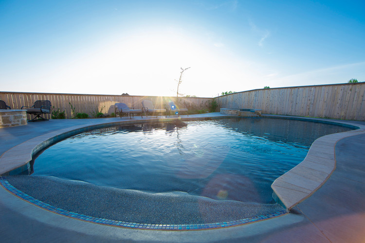 This is an example of a mid-sized beach style backyard round natural pool in Oklahoma City with a hot tub and natural stone pavers.