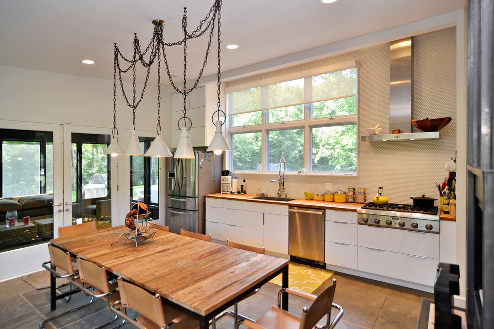 Photo of a small contemporary single-wall eat-in kitchen in Chicago with an undermount sink, flat-panel cabinets, white cabinets, wood benchtops, stainless steel appliances, white splashback, ceramic splashback and concrete floors.