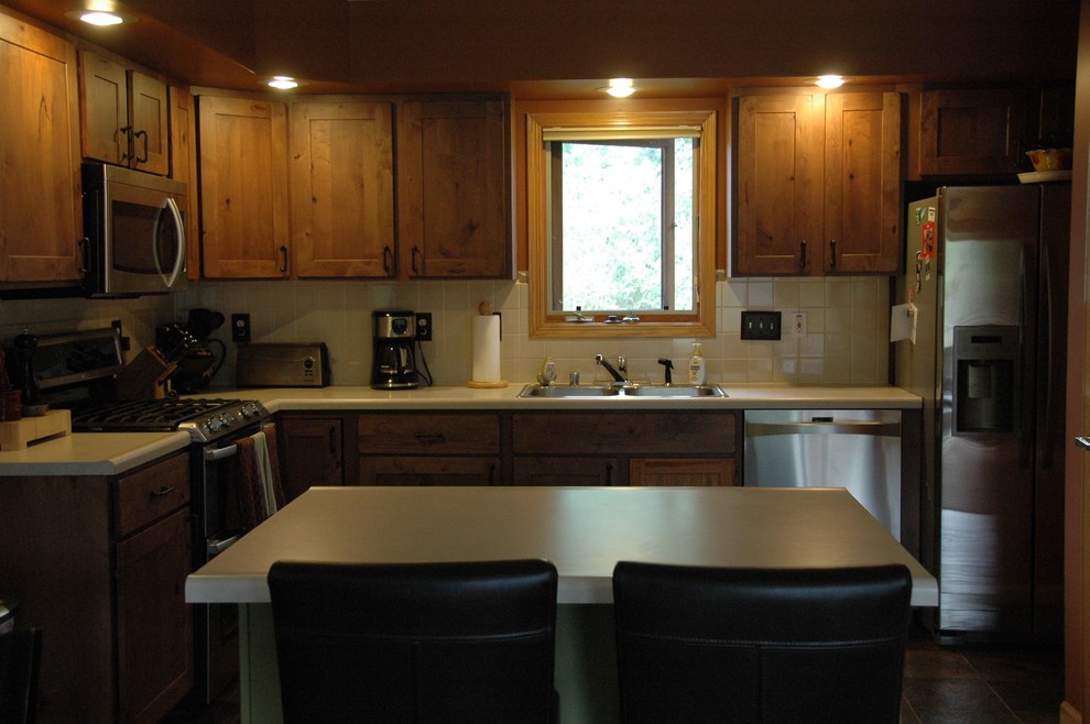 This is an example of a mid-sized traditional l-shaped eat-in kitchen in Denver with a double-bowl sink, shaker cabinets, medium wood cabinets, laminate benchtops, white splashback, ceramic splashback, stainless steel appliances, ceramic floors and with island.