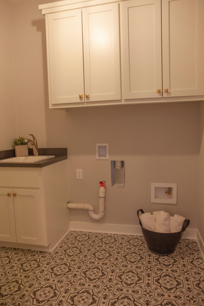 This is an example of a mid-sized arts and crafts single-wall dedicated laundry room in Minneapolis with a drop-in sink, shaker cabinets, white cabinets, laminate benchtops, grey walls, vinyl floors, a side-by-side washer and dryer, multi-coloured floor and grey benchtop.