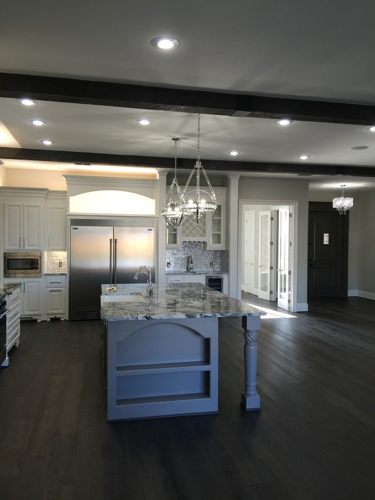 Mid-sized transitional l-shaped dark wood floor and brown floor open concept kitchen photo in Orange County with a farmhouse sink, raised-panel cabinets, white cabinets, marble countertops, metallic backsplash, metal backsplash, stainless steel appliances and an island