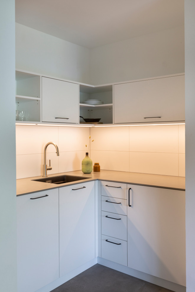 Inspiration for a small modern l-shaped open plan kitchen in Cologne with an undermount sink, flat-panel cabinets, white cabinets, solid surface benchtops, white splashback, ceramic splashback, stainless steel appliances, cement tiles, no island, grey floor, grey benchtop and wallpaper.